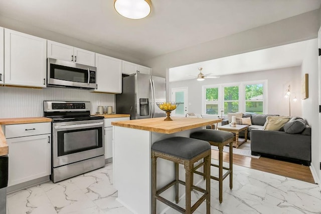 9811 Cambridge Ave, Kansas City, MO 64134 - kitchen featuring appliances with stainless steel finishes, butcher block countertops, light marble finish floors, and a breakfast bar