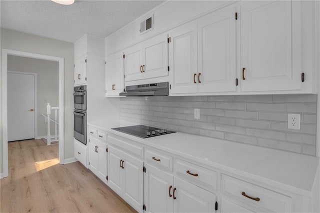 14 Woodbridge Ln, Kansas City, MO 64145 - kitchen featuring black electric stovetop, under cabinet range hood, light wood finished floors, white cabinetry, and a textured ceiling