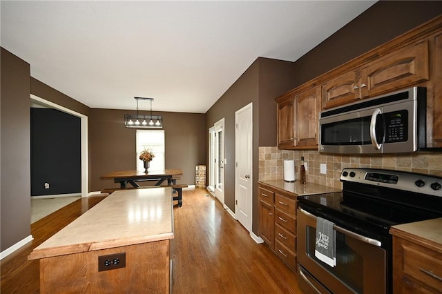 8941 NE 116th Pl, Kansas City, MO 64157 - kitchen with appliances with stainless steel finishes, dark wood-style flooring, backsplash, hanging light fixtures, and baseboards