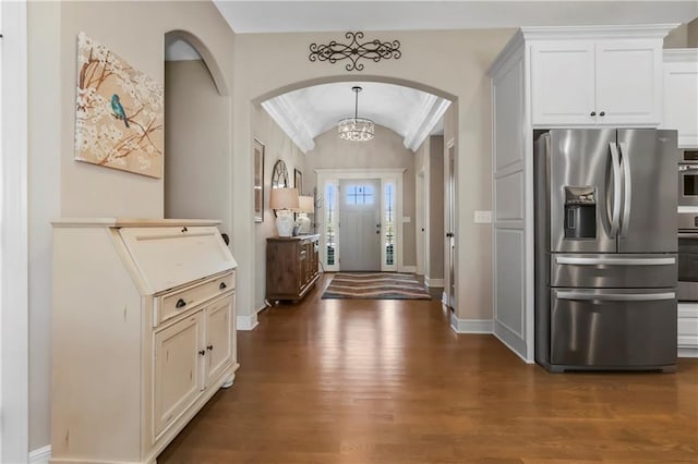 foyer featuring arched walkways, vaulted ceiling, dark wood finished floors, baseboards, and a chandelier