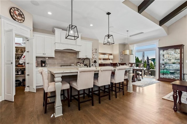 kitchen with dark wood finished floors, backsplash, an island with sink, white cabinets, and a breakfast bar