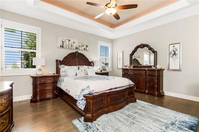 bedroom featuring a tray ceiling, dark wood-type flooring, multiple windows, and baseboards