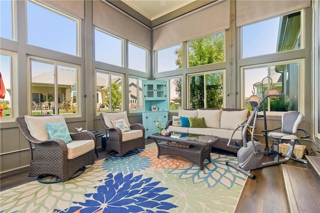 sunroom featuring wood-type flooring, a towering ceiling, and healthy amount of natural light