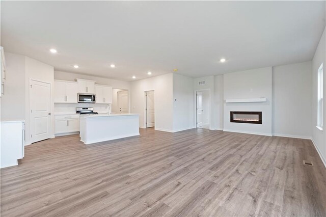 2114 Creek View Ln, Raymore, MO 64083 - unfurnished living room featuring light wood-style floors, recessed lighting, a glass covered fireplace, a sink, and baseboards