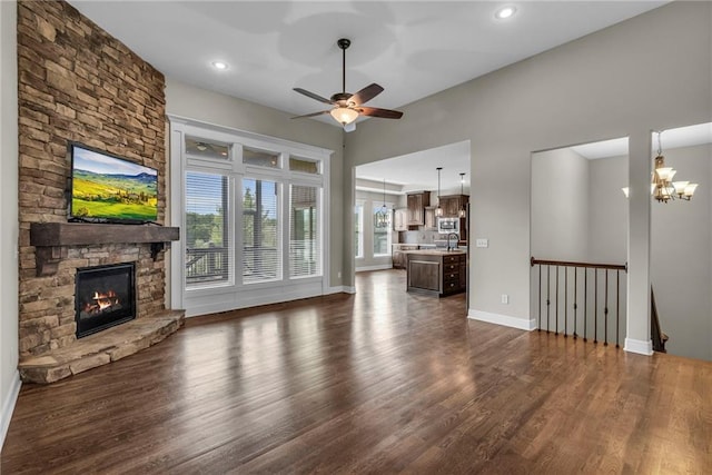 12750 N Arbor Way, Platte City, MO 64079 - unfurnished living room with dark wood-style flooring, ceiling fan, baseboards, a stone fireplace, and a chandelier