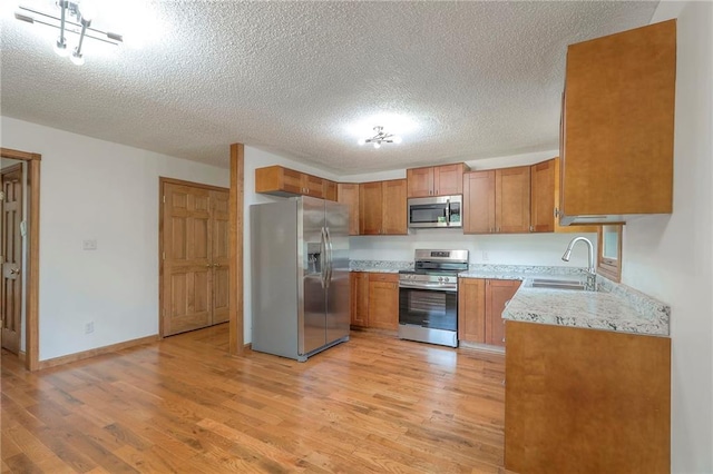 313 SW Ensley Ln, Lees Summit, MO 64081 - kitchen featuring stainless steel appliances, a sink, light wood finished floors, brown cabinets, and a textured ceiling