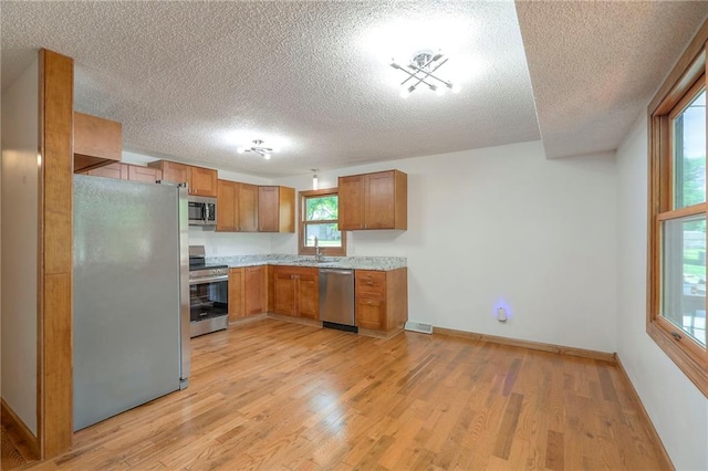 313 SW Ensley Ln, Lees Summit, MO 64081 - kitchen featuring appliances with stainless steel finishes, a textured ceiling, brown cabinetry, light wood-type flooring, and light countertops