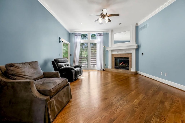 living room featuring crown molding, a ceiling fan, a tiled fireplace, wood finished floors, and baseboards