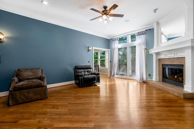 living area with a ceiling fan, crown molding, a fireplace, wood finished floors, and baseboards