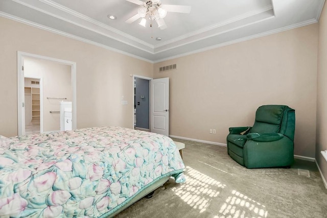 bedroom with carpet floors, a raised ceiling, ornamental molding, baseboards, and a walk in closet