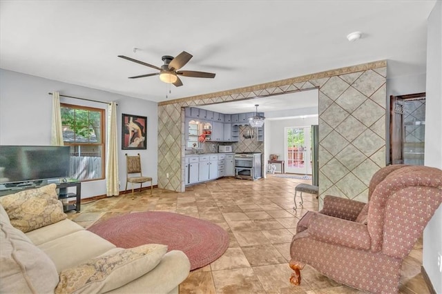 living area with a ceiling fan, healthy amount of natural light, an accent wall, and baseboards