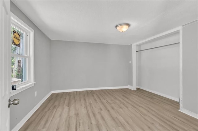 unfurnished bedroom featuring light wood finished floors, baseboards, and a closet