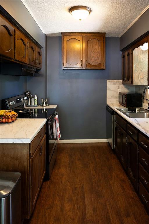108 N Evanston Ave, Independence, MO 64053 - kitchen featuring black appliances, a textured ceiling, dark wood-type flooring, light countertops, and under cabinet range hood