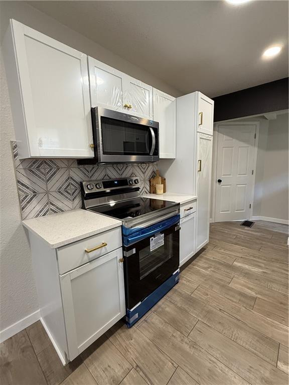 5715 Forest Ave, Kansas City, MO 64110 - kitchen with stainless steel microwave, electric stove, tasteful backsplash, and light countertops