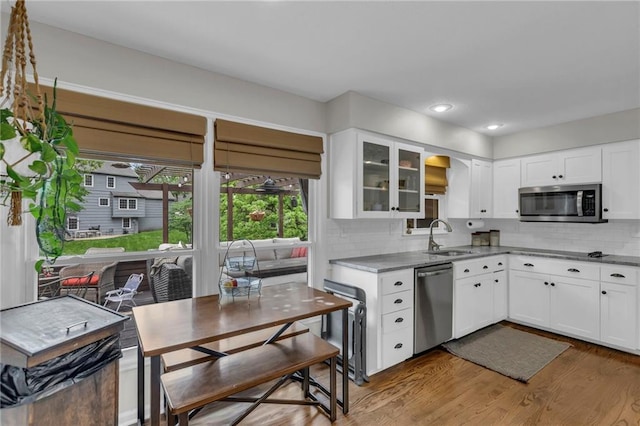 4212 NW Briarcliff Ln, Kansas City, MO 64116 - kitchen with stainless steel appliances, a sink, wood finished floors, tasteful backsplash, and glass insert cabinets