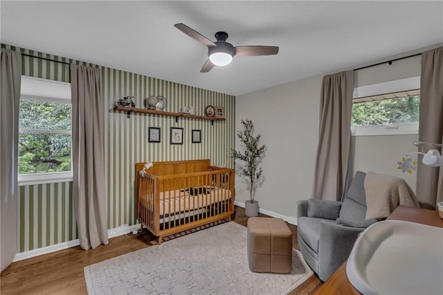 4212 NW Briarcliff Ln, Kansas City, MO 64116 - bedroom featuring wood finished floors, baseboards, a crib, ceiling fan, and wallpapered walls