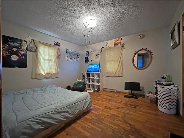 bedroom with wood finished floors, a textured ceiling, and baseboard heating