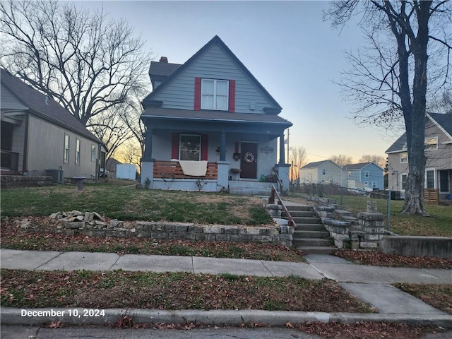 bungalow-style house featuring a chimney, covered porch, cooling unit, and a front lawn