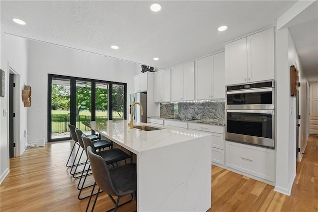 5263 SW Raintree Pkwy, Lees Summit, MO 64082 - kitchen with a sink, appliances with stainless steel finishes, light wood-type flooring, an island with sink, and decorative backsplash