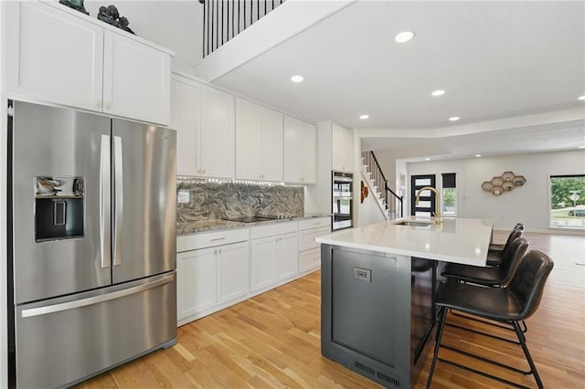 5263 SW Raintree Pkwy, Lees Summit, MO 64082 - kitchen featuring appliances with stainless steel finishes, a sink, white cabinets, light wood-style flooring, and backsplash