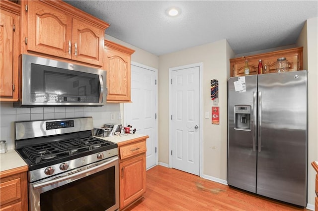 13825 Woodmont Ave, Bonner Springs, KS 66012 - kitchen featuring appliances with stainless steel finishes, light countertops, light wood-style floors, backsplash, and baseboards