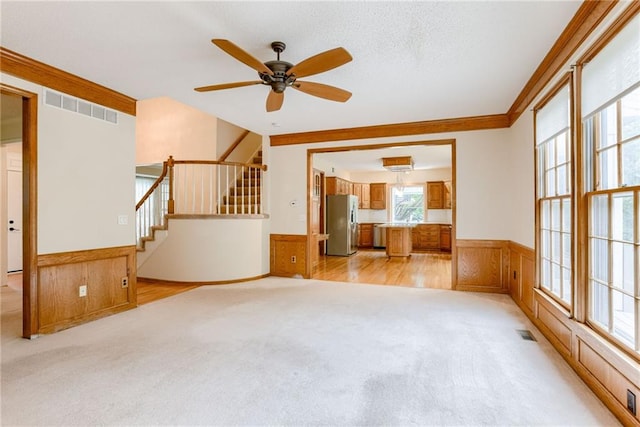 16482 W 132nd Cir, Olathe, KS 66062 - unfurnished living room featuring light colored carpet, wainscoting, stairway, ceiling fan, and wooden walls