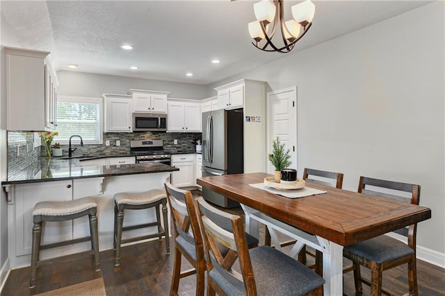 2511 E Maple Ct, Tonganoxie, KS 66086 - kitchen with appliances with stainless steel finishes, a peninsula, dark countertops, a sink, and decorative backsplash