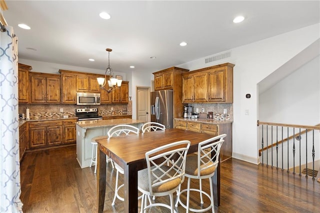 24318 W 91st Pl, Lenexa, KS 66227 - kitchen featuring stainless steel appliances, brown cabinetry, dark wood finished floors, a kitchen island, and recessed lighting