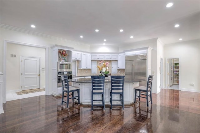 3109 W 118th St, Leawood, KS 66211 - kitchen featuring built in appliances, white cabinets, dark countertops, a kitchen breakfast bar, and a kitchen island