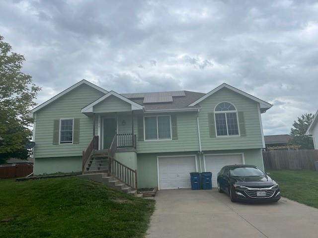 2216 Chanticleer St, Excelsior Springs, MO 64024 - view of front of house featuring an attached garage, roof mounted solar panels, and driveway