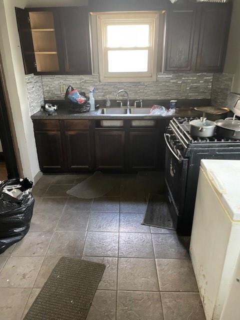 kitchen featuring backsplash, gas stove, a sink, and stone tile floors