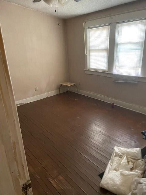 empty room featuring dark wood-style floors, a textured ceiling, a ceiling fan, and baseboards