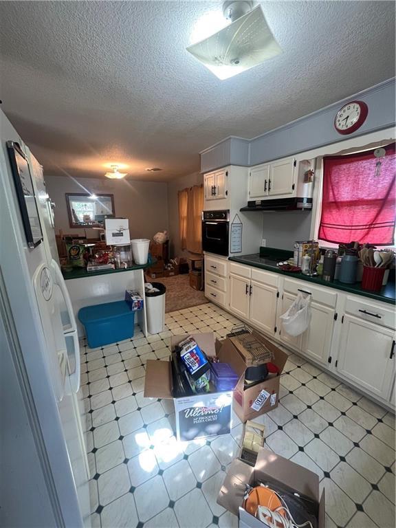 622 W Franklin St, Moran, KS 66755 - kitchen featuring black oven, a textured ceiling, dark countertops, white cabinets, and under cabinet range hood