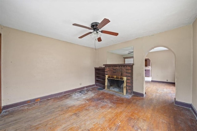 1111 S Cottage St, Independence, MO 64050 - unfurnished living room with wood-type flooring, a ceiling fan, a brick fireplace, baseboards, and arched walkways