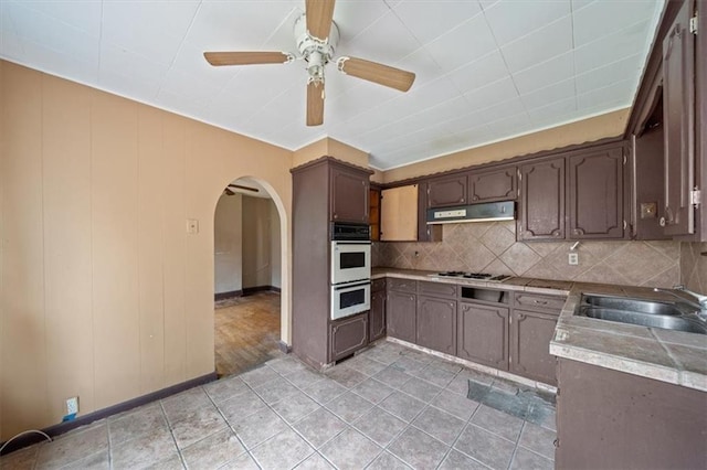 1111 S Cottage St, Independence, MO 64050 - kitchen featuring arched walkways, a sink, under cabinet range hood, a ceiling fan, and decorative backsplash
