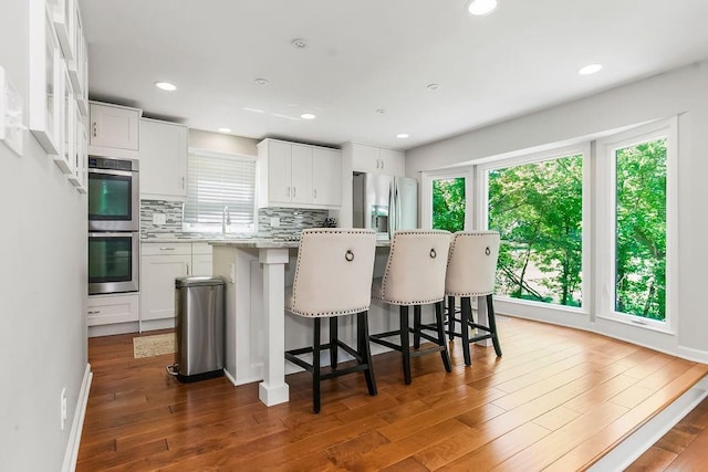 8911 W 104th St, Overland Park, KS 66212 - kitchen featuring a kitchen island, stainless steel appliances, decorative backsplash, white cabinetry, and a kitchen bar