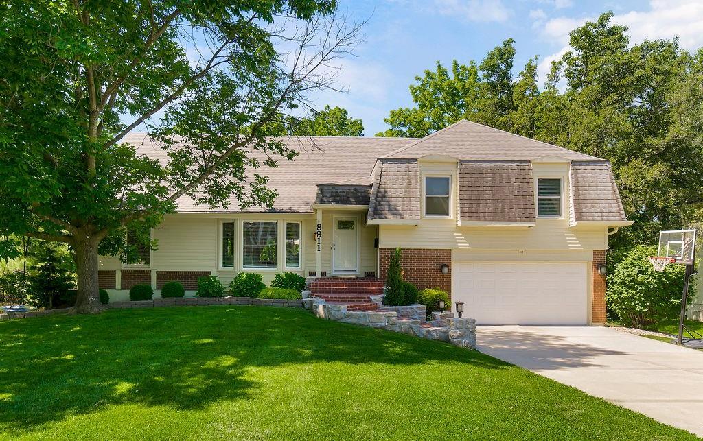 8911 W 104th St, Overland Park, KS 66212 - tri-level home featuring brick siding, roof with shingles, concrete driveway, and an attached garage