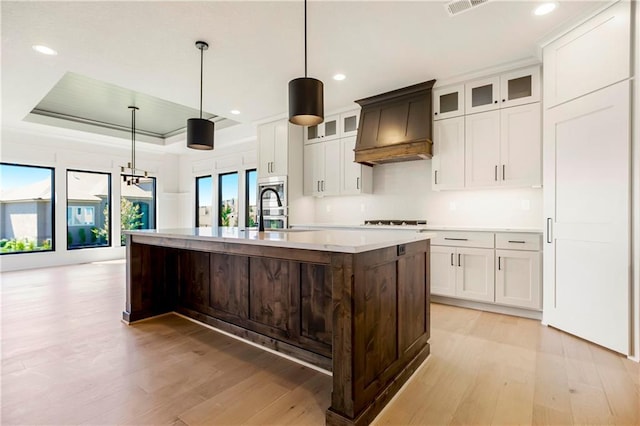 17556 Acton St, Overland Park, KS 66085 - kitchen with a sink, custom exhaust hood, light wood-type flooring, light countertops, and a center island with sink
