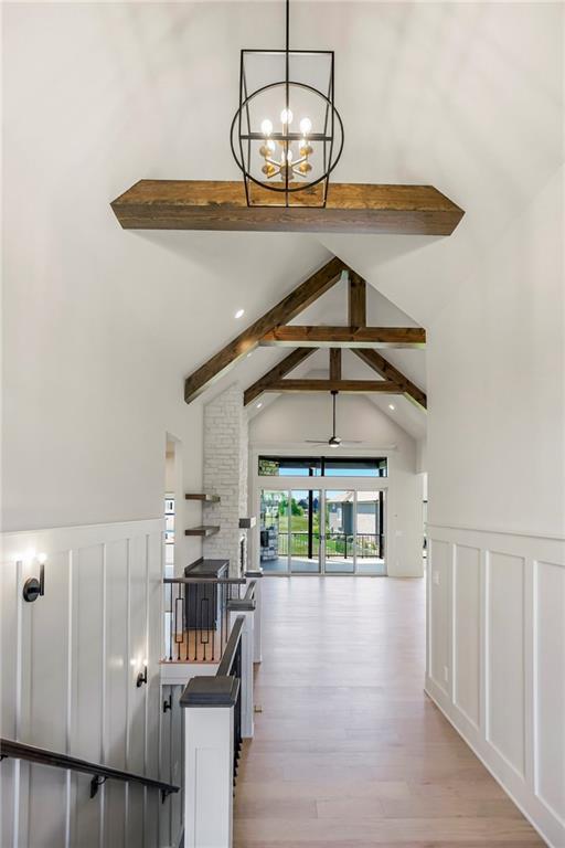17556 Acton St, Overland Park, KS 66085 - hallway featuring beam ceiling, a chandelier, a decorative wall, wainscoting, and light wood-style flooring