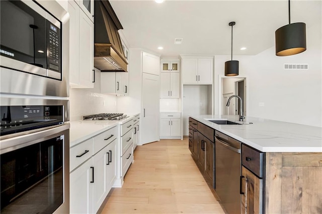 17556 Acton St, Overland Park, KS 66085 - kitchen featuring stainless steel appliances, a sink, premium range hood, light wood-style floors, and glass insert cabinets