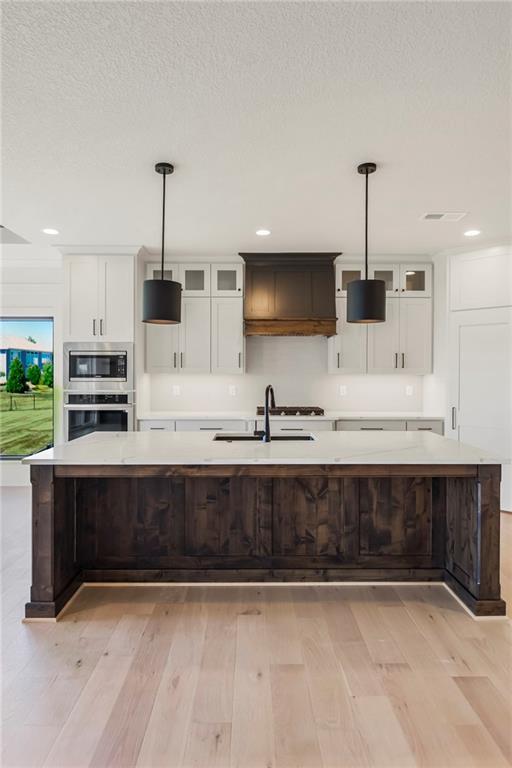 17556 Acton St, Overland Park, KS 66085 - kitchen featuring light wood-style flooring, light countertops, a sink, a large island, and white cabinets