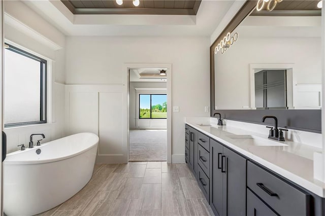 17556 Acton St, Overland Park, KS 66085 - bathroom featuring a raised ceiling, double vanity, a freestanding tub, and wainscoting