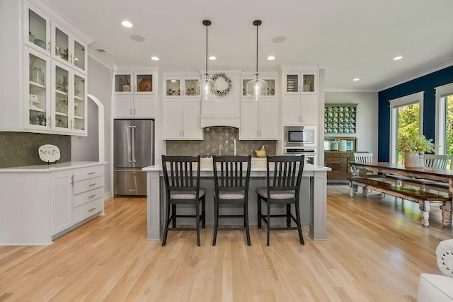 9305 SW Sushi Cir, Lees Summit, MO 64064 - kitchen featuring stainless steel appliances, ornamental molding, backsplash, light wood-style flooring, and white cabinetry