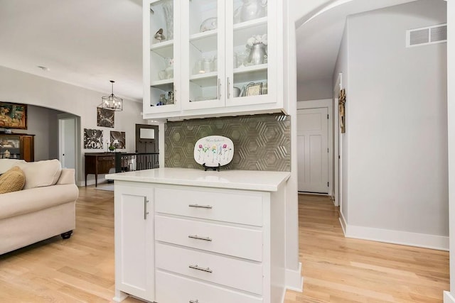 9305 SW Sushi Cir, Lees Summit, MO 64064 - kitchen featuring arched walkways, light wood-style flooring, white cabinetry, glass insert cabinets, and light countertops
