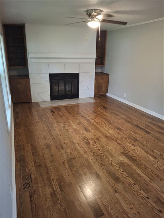715 E Blackhawk St, Ottawa, KS 66067 - unfurnished living room featuring wood finished floors, a tiled fireplace, ceiling fan, and baseboards