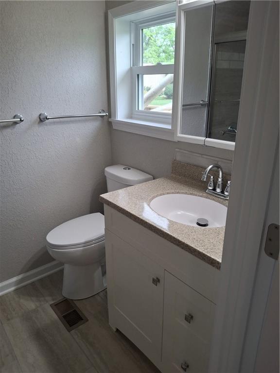 715 E Blackhawk St, Ottawa, KS 66067 - bathroom with wood finished floors, toilet, vanity, a textured wall, and baseboards