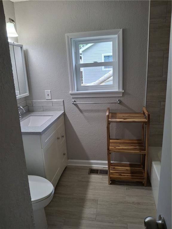 715 E Blackhawk St, Ottawa, KS 66067 - bathroom featuring vanity, baseboards, a textured wall, toilet, and a tub to relax in
