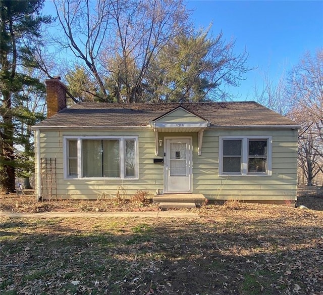 bungalow featuring a chimney and a shingled roof