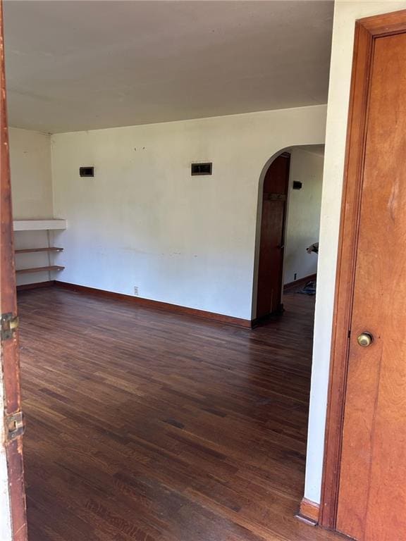 unfurnished room with arched walkways, dark wood-style floors, and baseboards