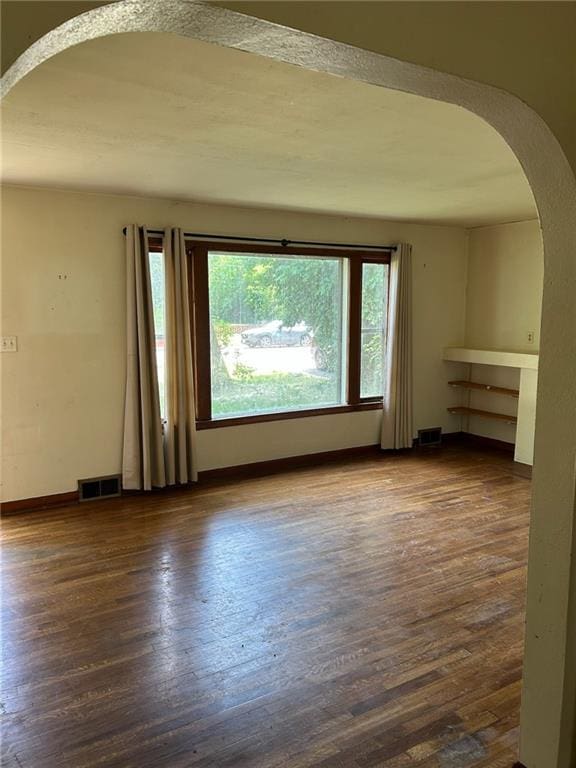 unfurnished room with arched walkways, healthy amount of natural light, and dark wood-style floors